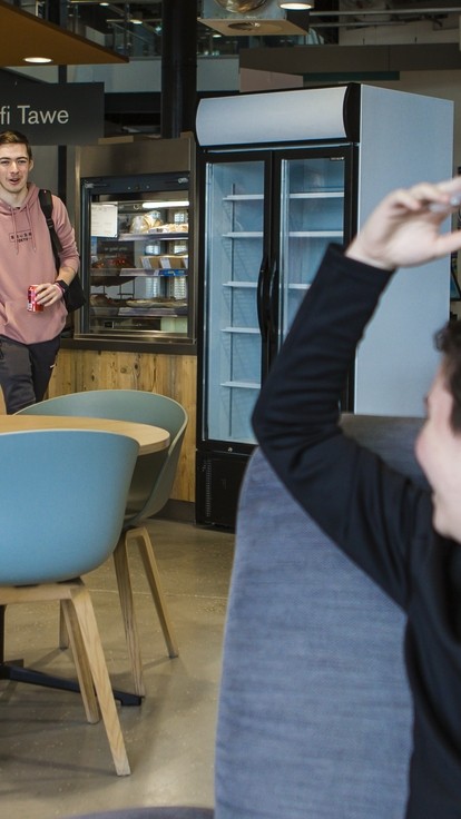 student waving at friends inside swansea campus cafe