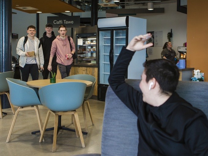student waving at friends inside swansea campus cafe