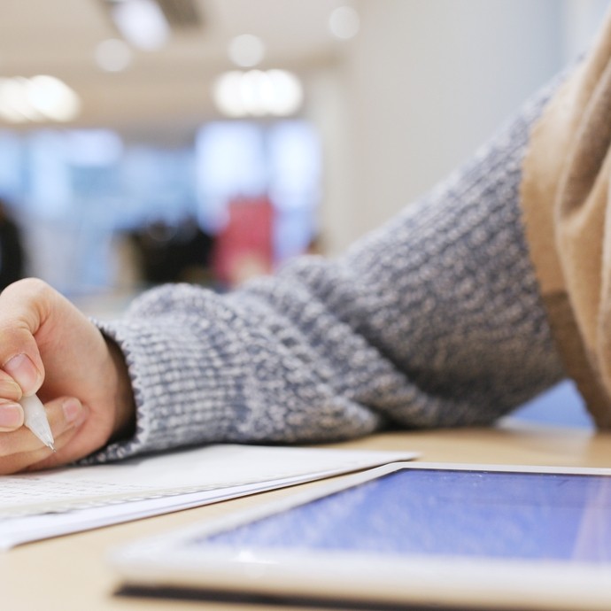 Student working on a tablet and writing on a notepad