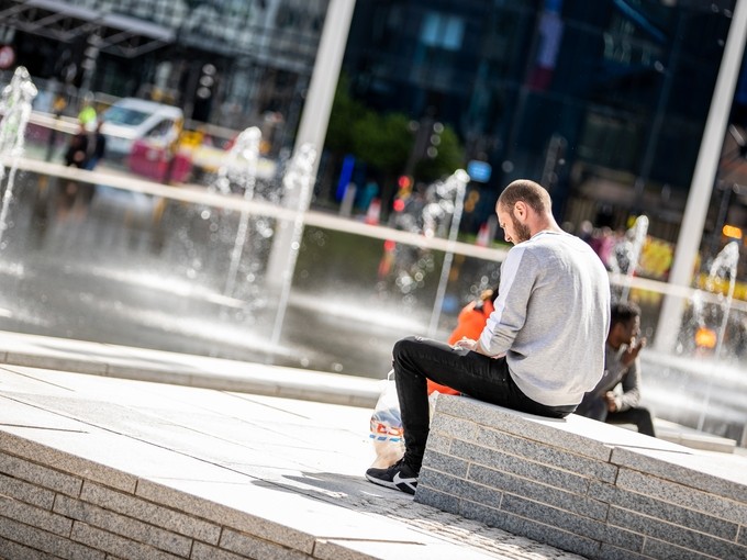 Person sitting down on concrete ledge surrounded by fountains