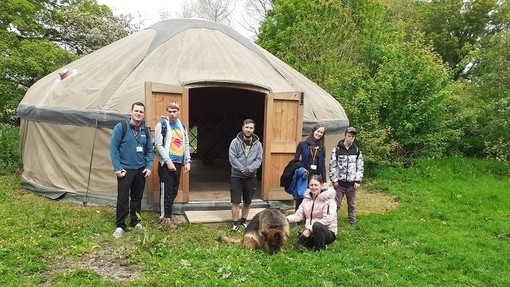 Some people and a German Shepherd Dog outside a large yurt.