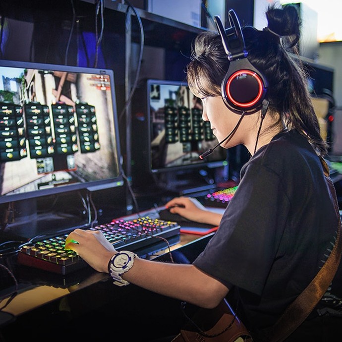 A young female student wearing headphones works at a glowing keyboard and monitor.