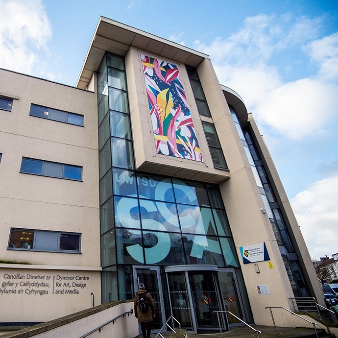 A modern building with multiple glass panels extending from the entrance doors to the roof and reading SCA.