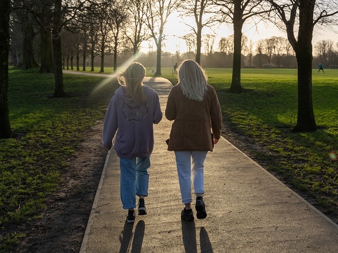 Two people walking along a path with the sun shining through the trees