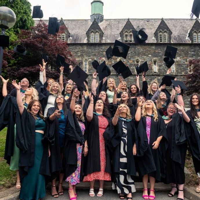 Graduating students throw their mortarboard hats in the air in front of the Old College, Carmarthen.
