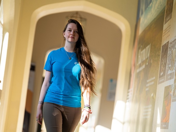 Student wearing a blue shirt walking down a corridor