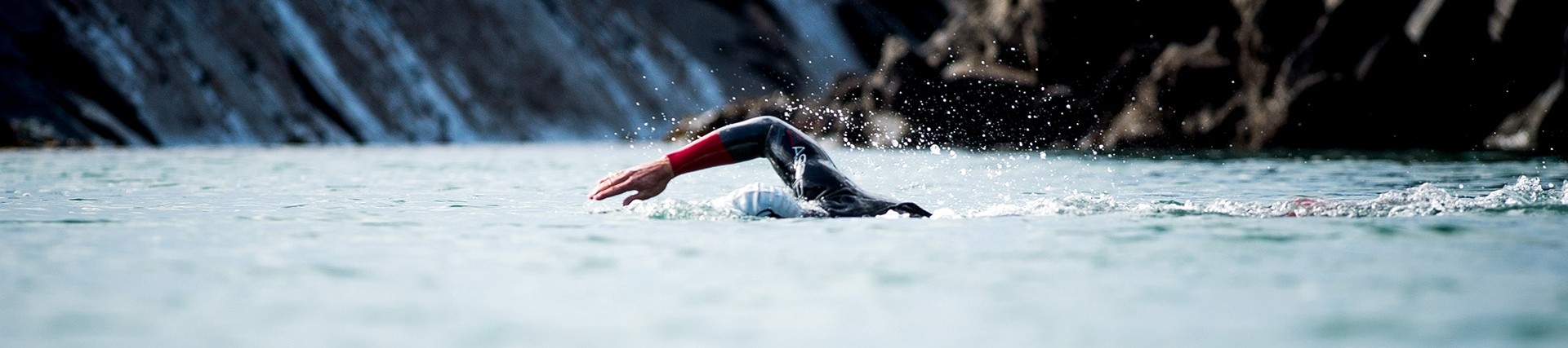 A rocky bay with a man swimming through the water in a wetsuit.