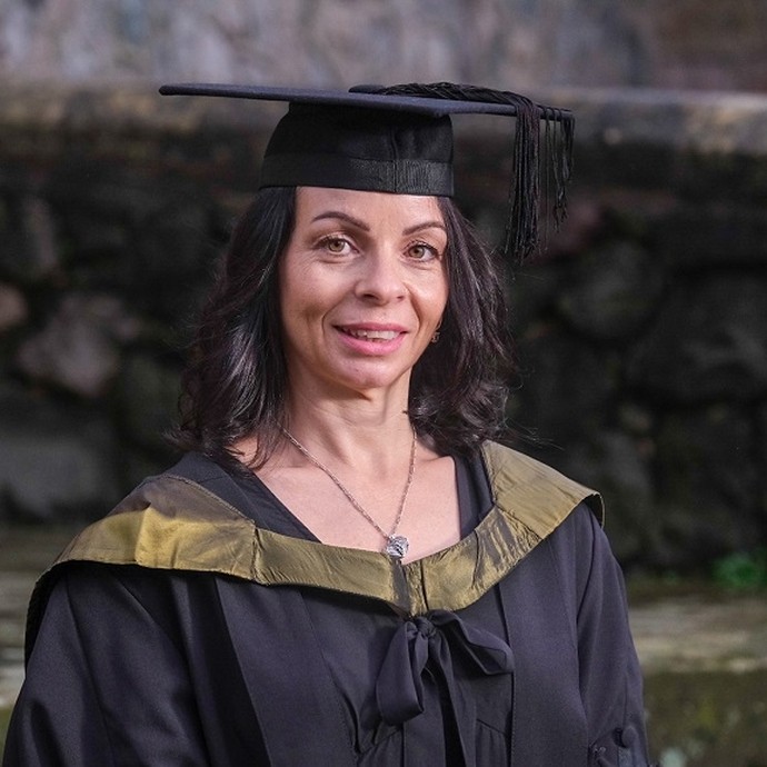 Emma Williams smiles slightly while wearing an academic hat and gown with a golden hood.